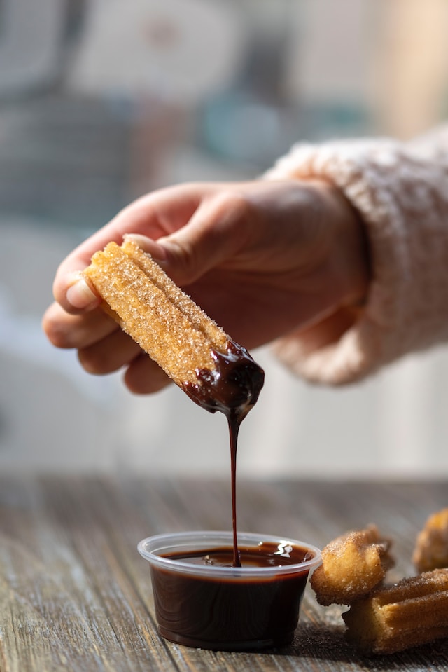 hand dipping a piece of churros in chocolate sauce