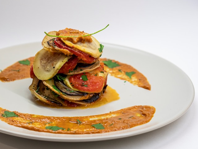 A stack of sliced vegetables served with orange sauce on a white plate