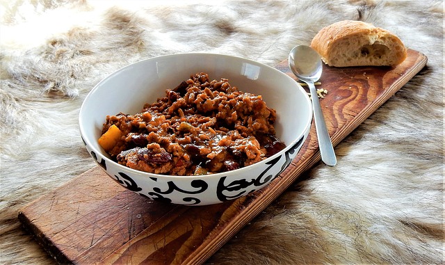 Chili con carne on a ceramic bowl served with a slice of toast on a wooden board