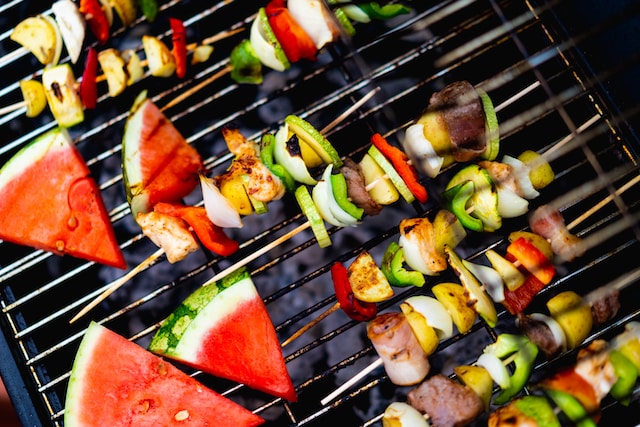 Meat and vegetables skewers and slices of water melon on a charcoal grill
