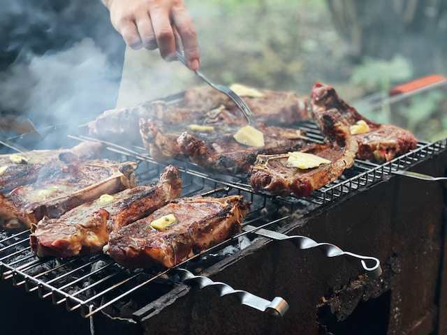 A person adding butter to meat cooking on grill