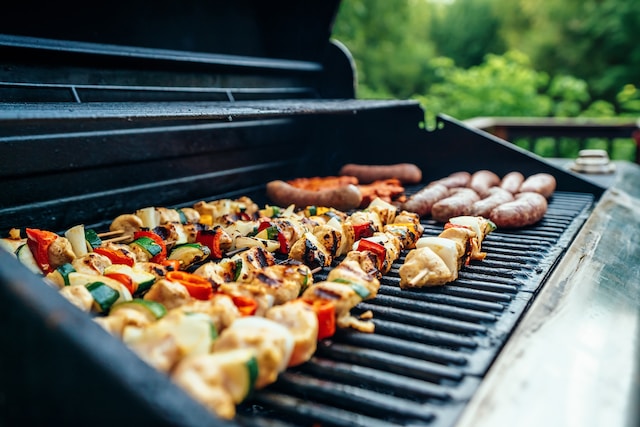 vegetable and meat skewers and sausages cooking on a grill