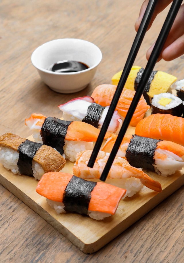 Assorted sushi on a wooden board served with a soy sauce dip