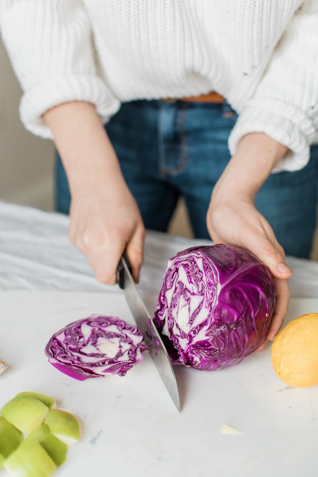 Person chopping a purple cabbage on a white surface
