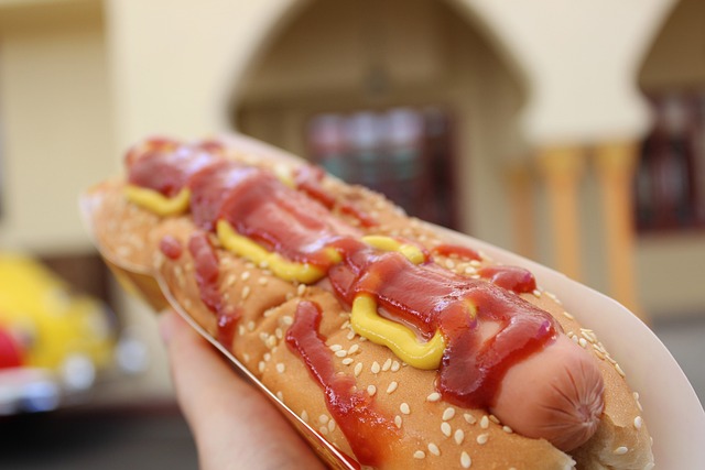 Hand holding a hotdog in a bun drizzled with mustard and ketchup