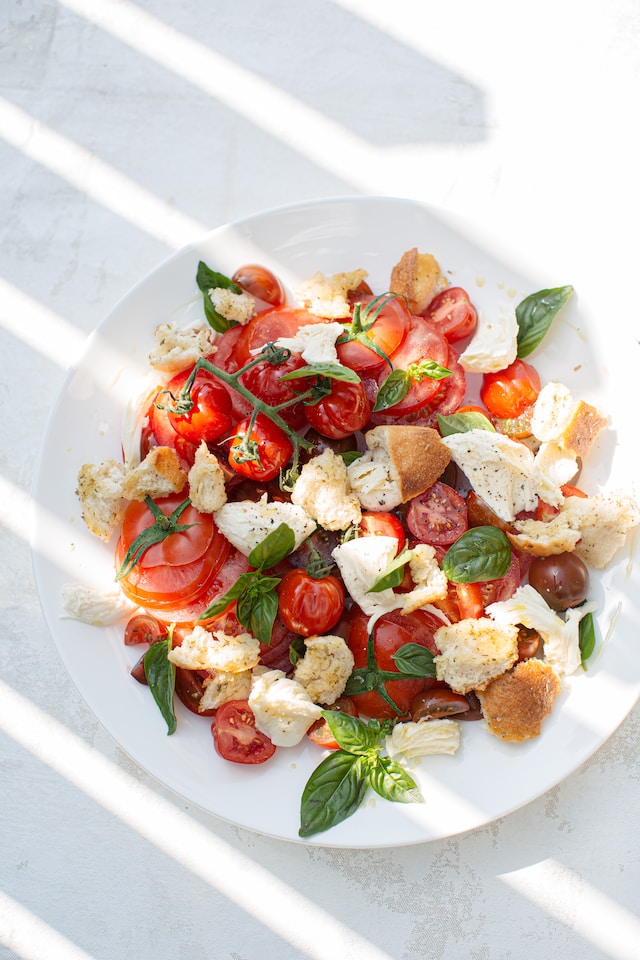 Sliced tomatoes, basil leaves, croutons, and pieces of cheese served on a white plate