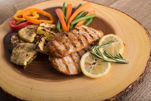 Grilled chicken breasts served with assorted grilled veggies on a wooden board