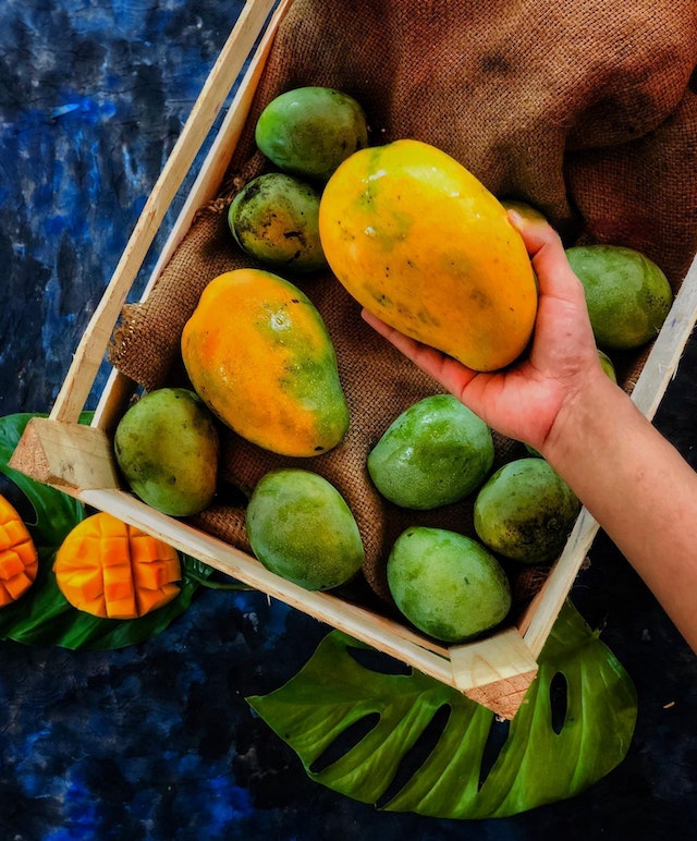 A hand picking up a ripe mango from a wooden crate