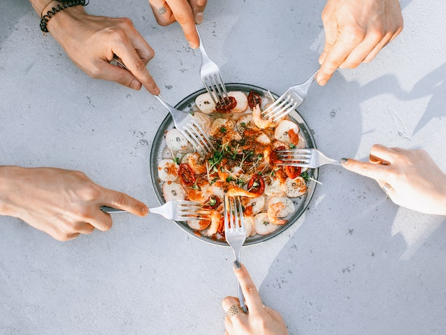 Hands holding fork dipping into a plate of shrimps