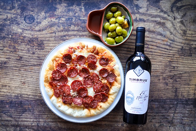 Pizza, a bottle of wine, and a dish of olives on a wooden surface