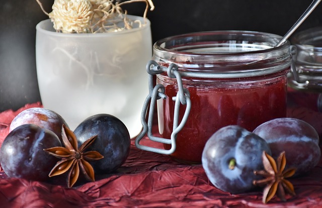 An open jar of jam surrounded by plums