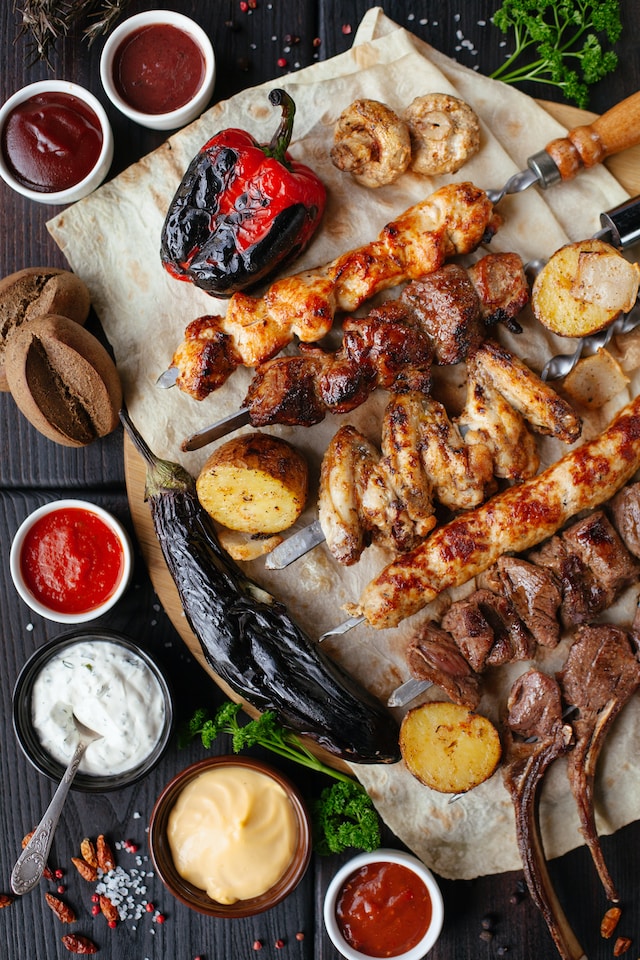 Assorted meat on skewers, grilled vegetables, brown bread and a variety of dips on a table