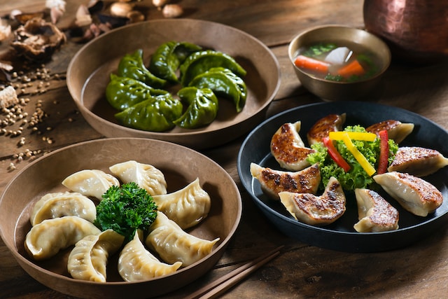 Assorted dumplings on ceramic plates with a small bowl of soup on the side