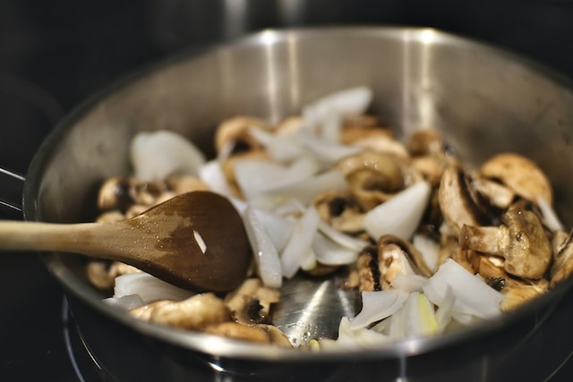 Person cooking mushrooms nd onions in a steel pan