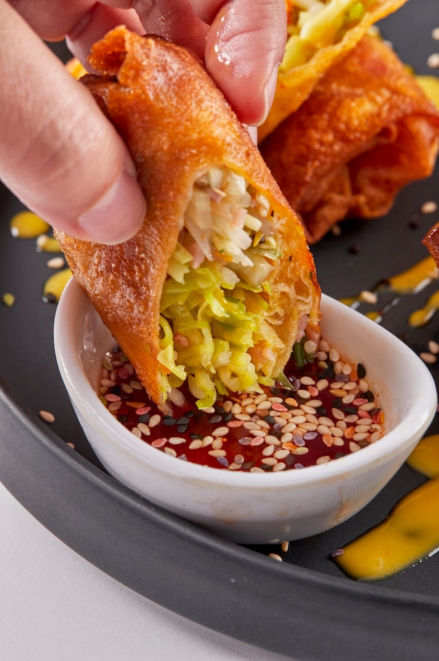Hand dipping spring roll into sauce