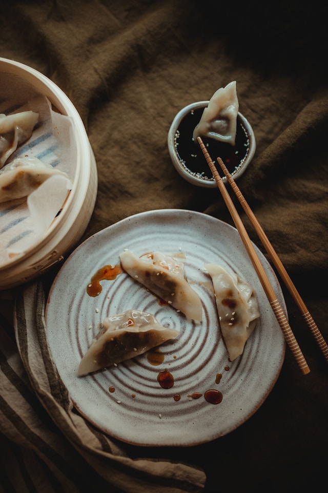 Steamed dumplings on a ceramic plate with one piece dipped in sauce