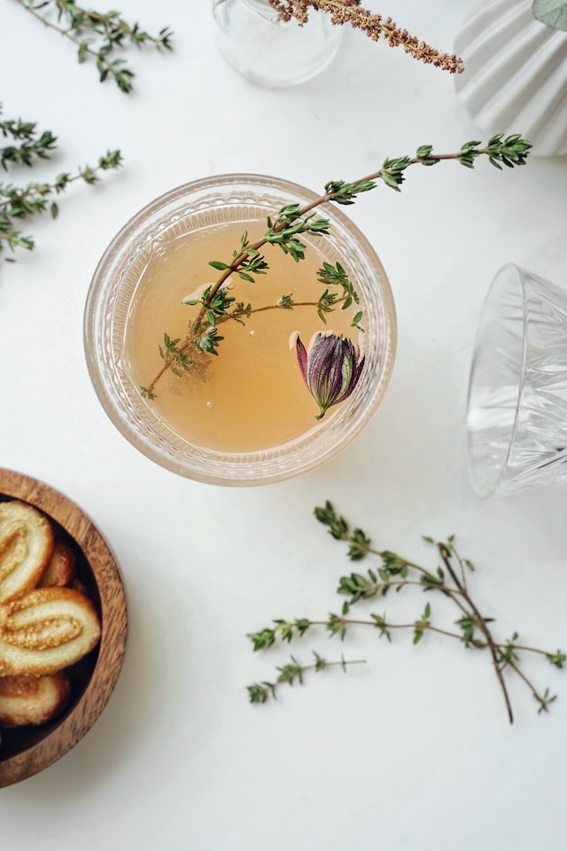 Drink inside a clear glass garnished with with some thyme 