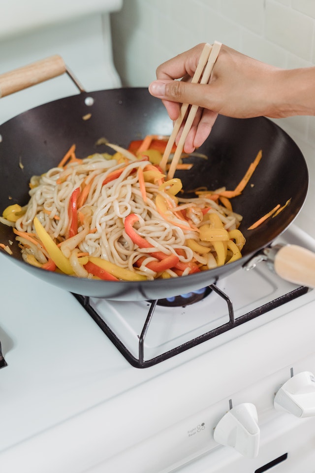 Person cooking noodles in a wok