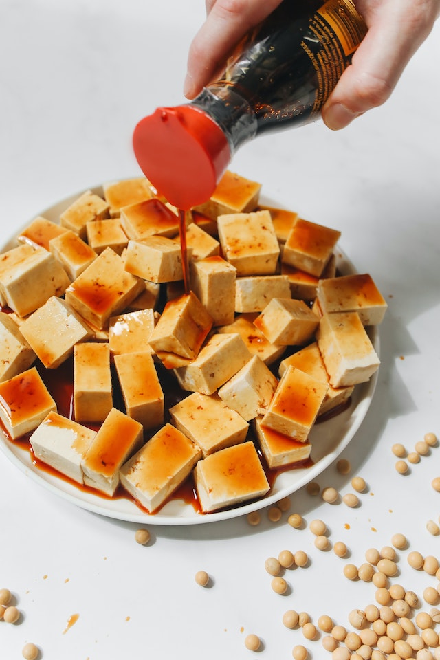 Hand pouring soy sauce on cubed tofu