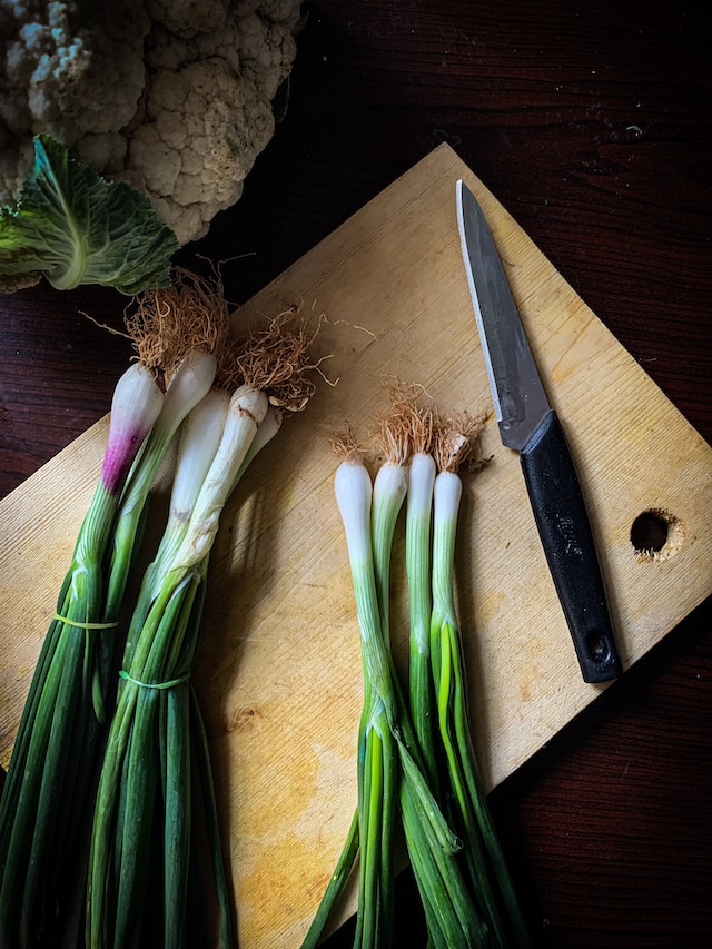 Spring onions and a knife on a wooden chopping board