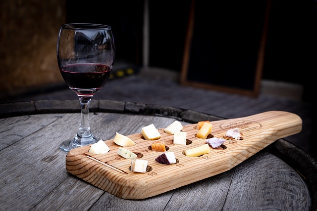 Assorted cheese slices on a wooden board with a glass of red wine on the side