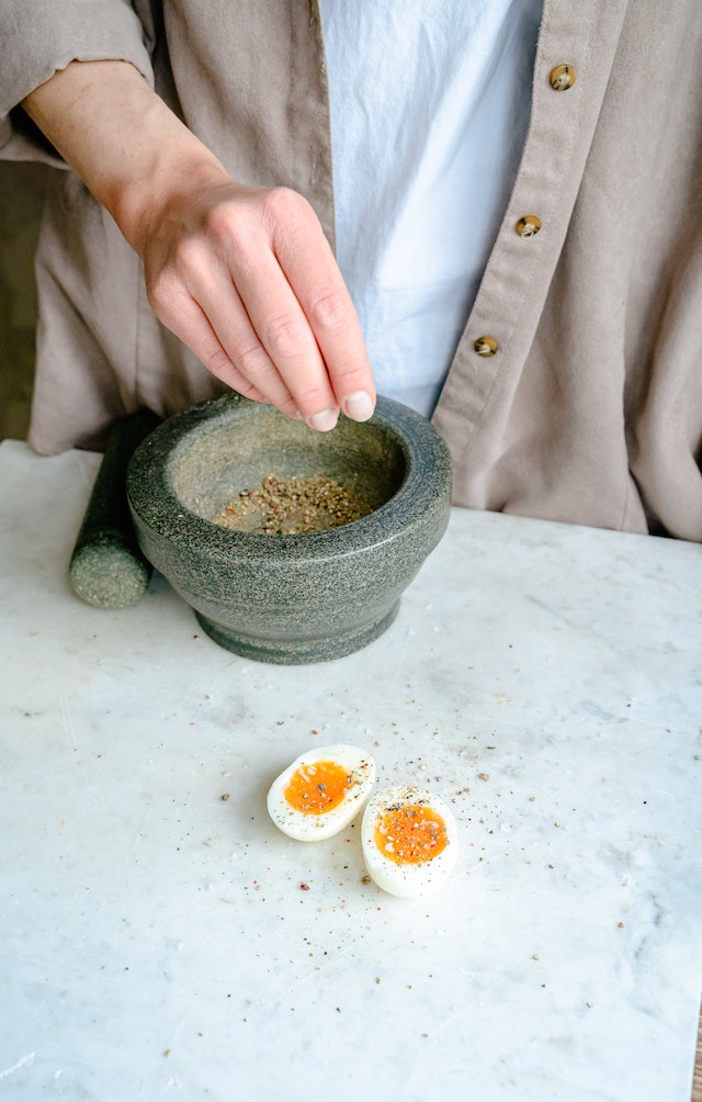Person sprinkling freshly ground pepper onto two slices of boiled egg