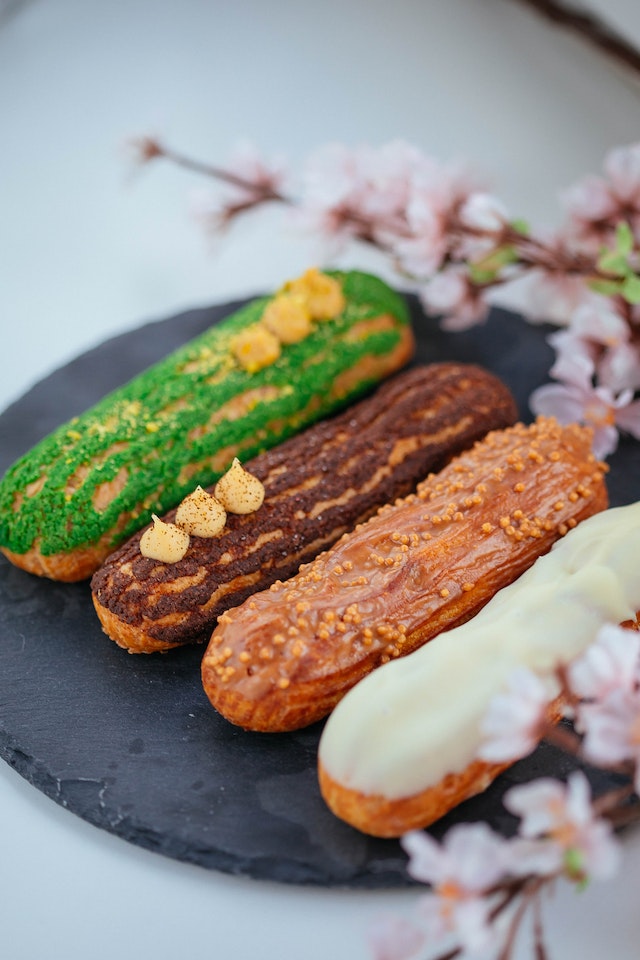 Different flavored eclairs on a black, flat ceramic plate