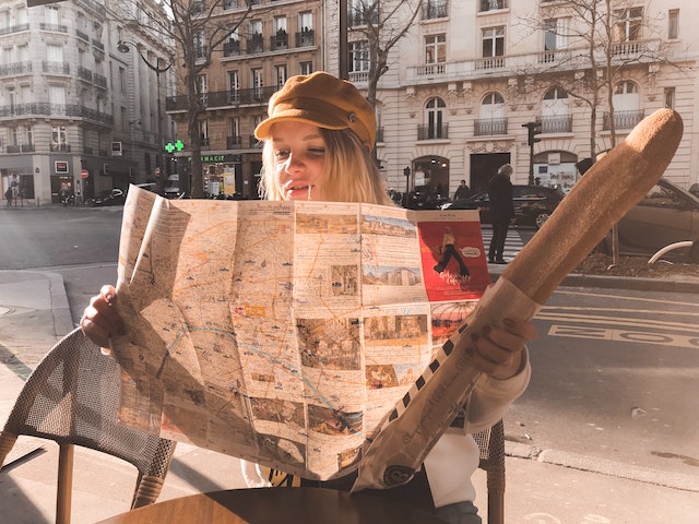 Person reading a map and holding a baguette