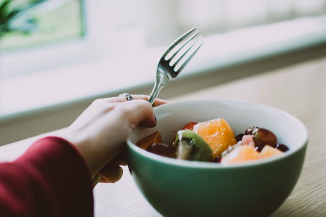 Person holding a fork and a bowl filled with assorted sliced fruits