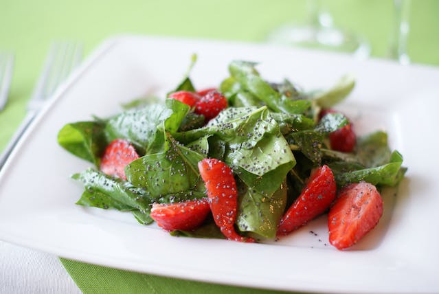 A salad of greens and strawberry slices on a white ceramic plate