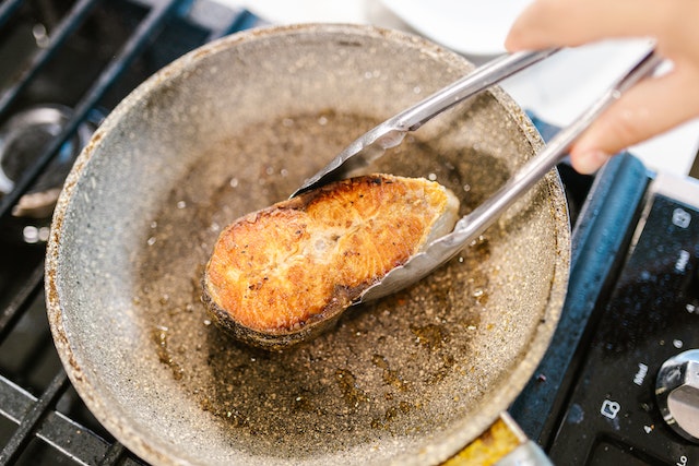 Person cooking fish in a pan